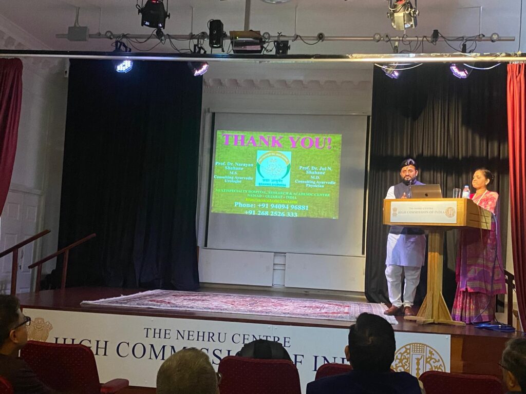 A presentation at the Nehru Centre, featuring two speakers at a podium. A 'Thank You' slide is projected in the background, displaying contact details for Prof. Dr. Narayan Shubhan and Prof. Dr. Jit N. Shubhan. The audience is visible in the foreground.